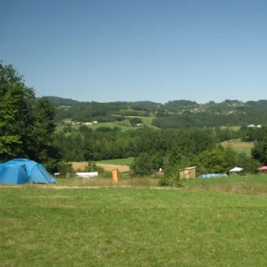 Groene weide met tenten en heuvelachtig landschap op de achtergrond.